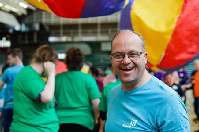 Mann schaut in die Kamera. Hinter ihm fliegen große, bunte Bälle