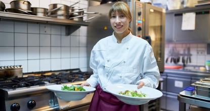 Eine Auszubildende in der Gastronomie bringt die Speisen aus der Küche zu den Gästen