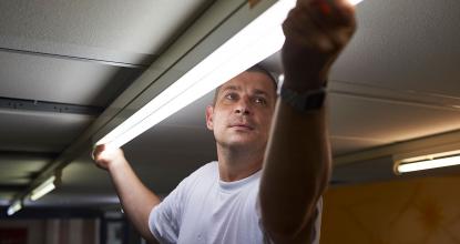 Ein Mitarbeiter im Gebäudeservice wechselt eine Röhrenlampe