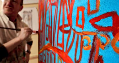 Künstler der Kunstwerkstatt Mosaik Berlin mit Pinsel steht vor seinem Gemälde in Rot und Blau