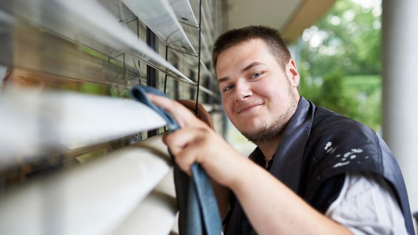 Eine  Mitarbeiter der Gebäudereinigung von Mosaik reinigt die Lamellen der Außenjalousie